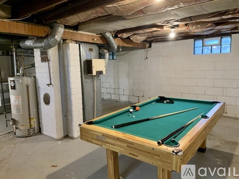 A pool table in a basement with a green felt top and white cushions.