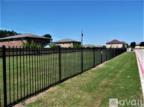 A black metal fence runs along a grassy area in front of a row of houses.