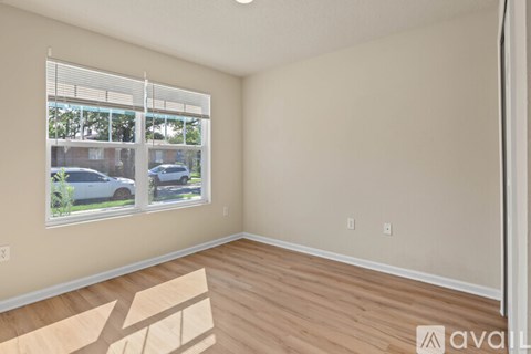 A room with wooden flooring and a window showing a view of cars and trees outside.