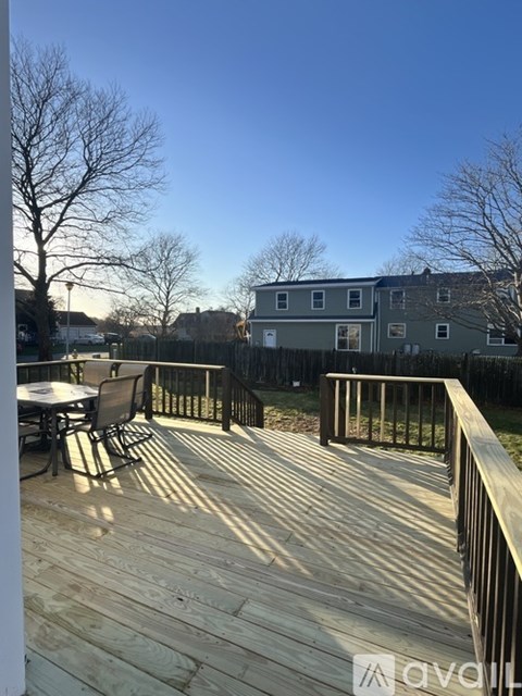 A wooden deck with a table and chairs is in the foreground with a house and trees in the background.