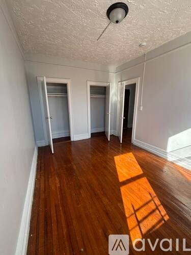 A room with wooden floors and white walls, with a window casting a shadow on the floor.