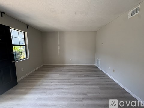 A spacious room with a black door and a window on the left side.