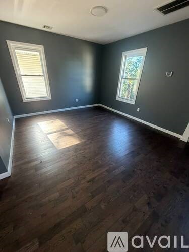 A room with wooden flooring and two windows.