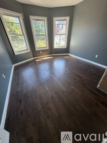 A room with wooden flooring and three windows.