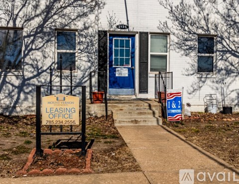 A leasing office sign is in front of a white building with a blue door.