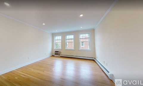 A spacious room with wooden flooring and two windows.