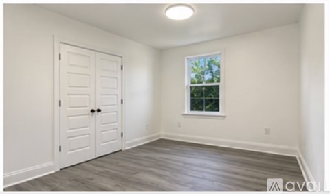A room with a white door and a window with a view of trees outside.