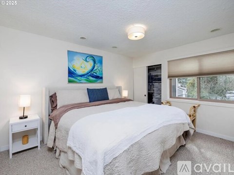 A bedroom with a large bed, a nightstand with a lamp, and a painting on the wall.
