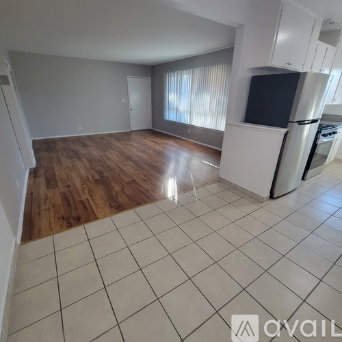 A spacious living room with wooden floors and a kitchen area with white cabinets and appliances.