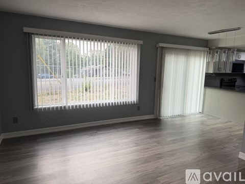 A spacious room with a large window and wooden flooring.