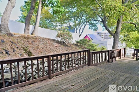 A wooden deck with railings overlooks a hill with trees and a building in the distance.