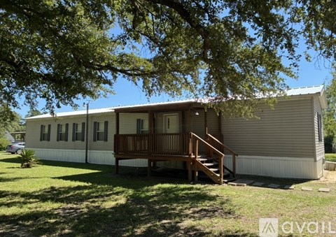 A mobile home with a deck and a carport is surrounded by trees.