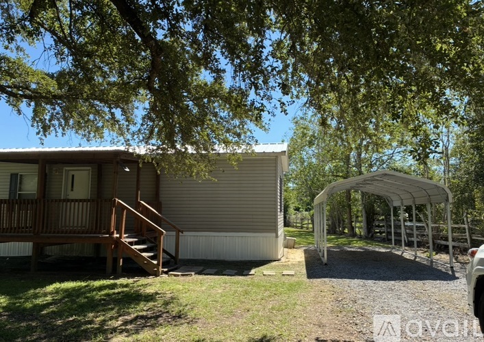 A house with a porch and a carport is surrounded by trees.