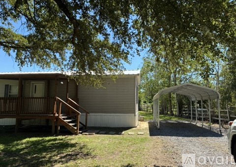 A house with a porch and a carport is surrounded by trees.