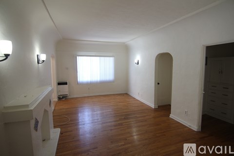 A room with wooden floors and white walls, with a window covered by white blinds.