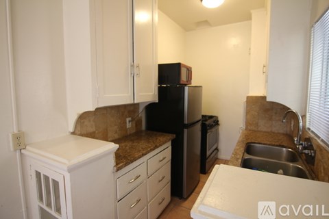 A kitchen with a black fridge, white cabinets, and a brown counter.