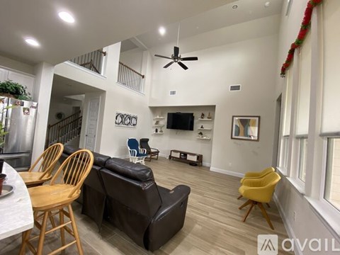 A living room with a black couch, wooden chairs, and a ceiling fan.