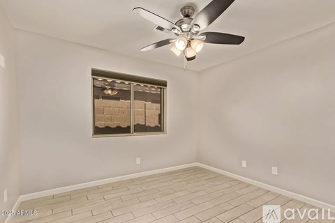 A room with a ceiling fan and a window with a view of a building.