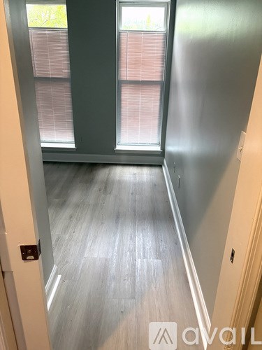 A hallway with a wooden floor and a window with blinds.