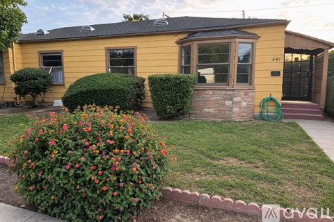 A yellow house with a green hose on the front porch.