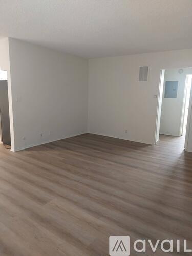 A room with wooden flooring and white walls, with a door on the right side.