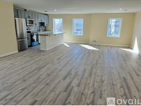 A spacious kitchen with wooden flooring and a refrigerator.