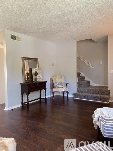 A living room with a wooden floor and a staircase in the background.