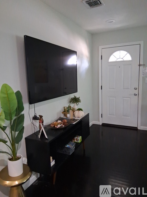 A black television is mounted on a white wall above a black piano.
