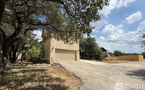 A house with a garage is surrounded by trees and has a fence in the background.