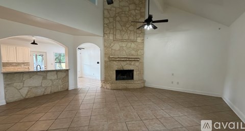 A spacious living room with a stone fireplace and a fan.
