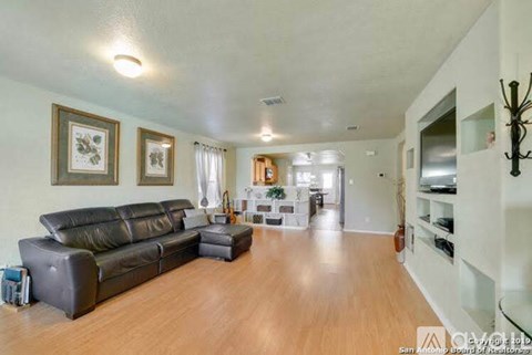 A living room with a black leather couch and wooden floors.
