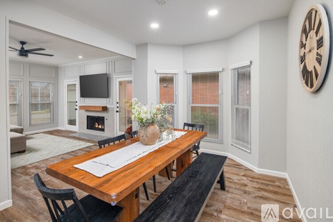 A modern dining room with a wooden table and bench, a television, and a fireplace.