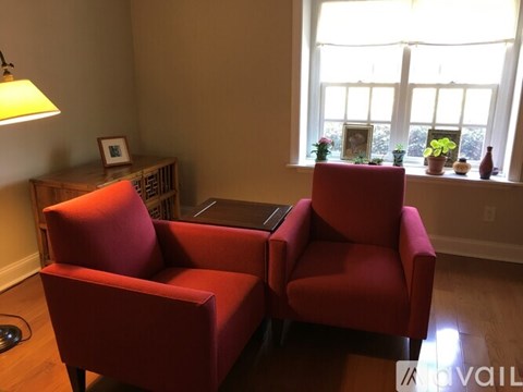 Two red chairs in front of a window with a lamp on the side table.