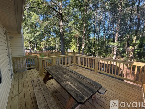 A wooden table is on a deck with a railing and trees in the background.
