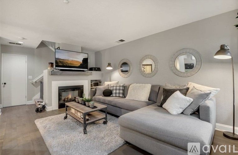 A modern living room with a grey couch, a fireplace, and a television mounted above it.