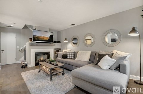 A modern living room with a grey couch, a fireplace, and a television mounted above it.