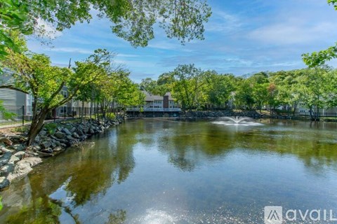 A serene pond surrounded by lush greenery and a fence with a house in the background.