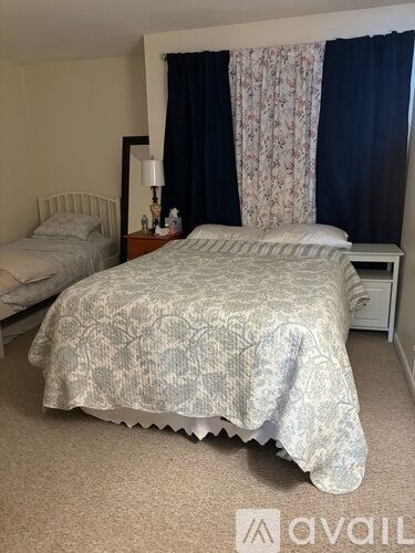A bedroom with a bed covered in a grey floral bedspread.