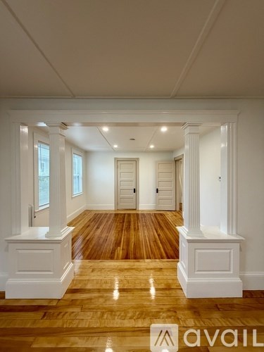 A spacious hallway with wooden floors and white walls.