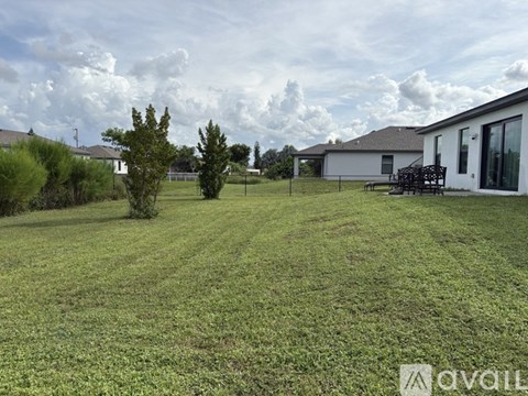A grassy field with a house and trees in the background.