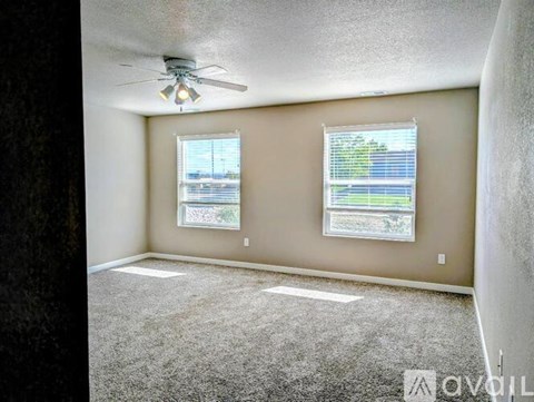 A room with a ceiling fan and two windows.