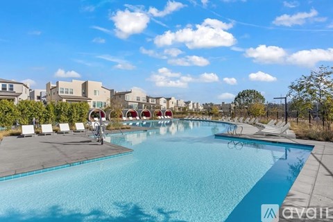 A large outdoor swimming pool surrounded by lounge chairs and buildings in the background.