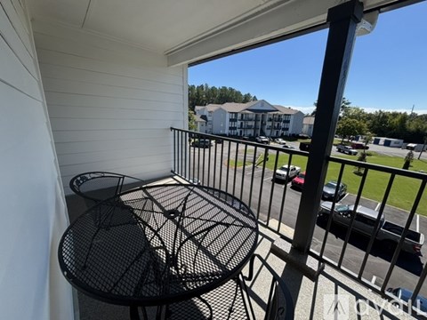 A balcony with a table and chairs overlooks a parking lot.