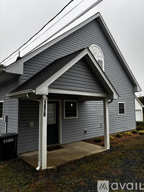 A house with a grey siding and a black door is available for rent.