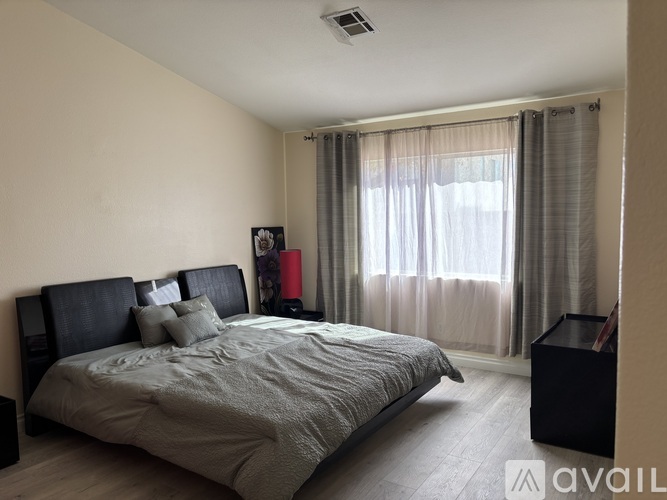 A bedroom with a large bed and a window with curtains.