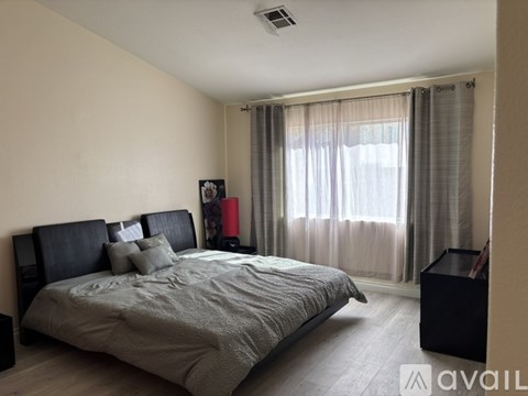 A bedroom with a large bed and a window with curtains.