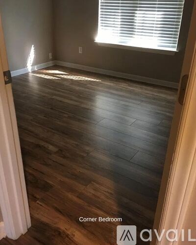 A corner bedroom with wooden flooring and a window with blinds.