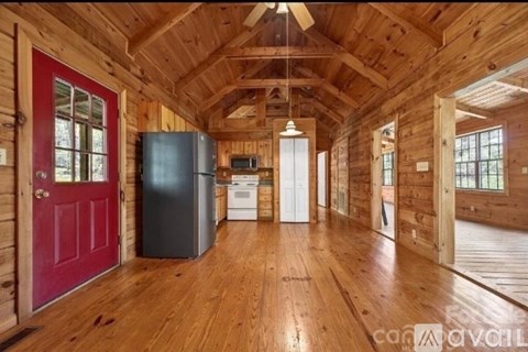 A spacious wooden interior of a house with a red door and a black refrigerator.
