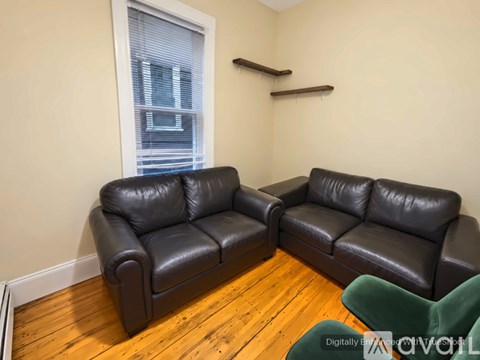 Two black leather sofas in a room with wooden flooring and a window.