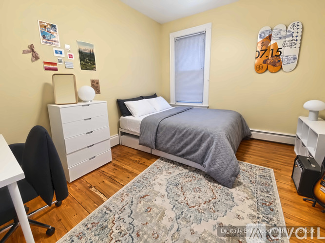 A bedroom with a bed, desk, chair, and a rug on the floor.